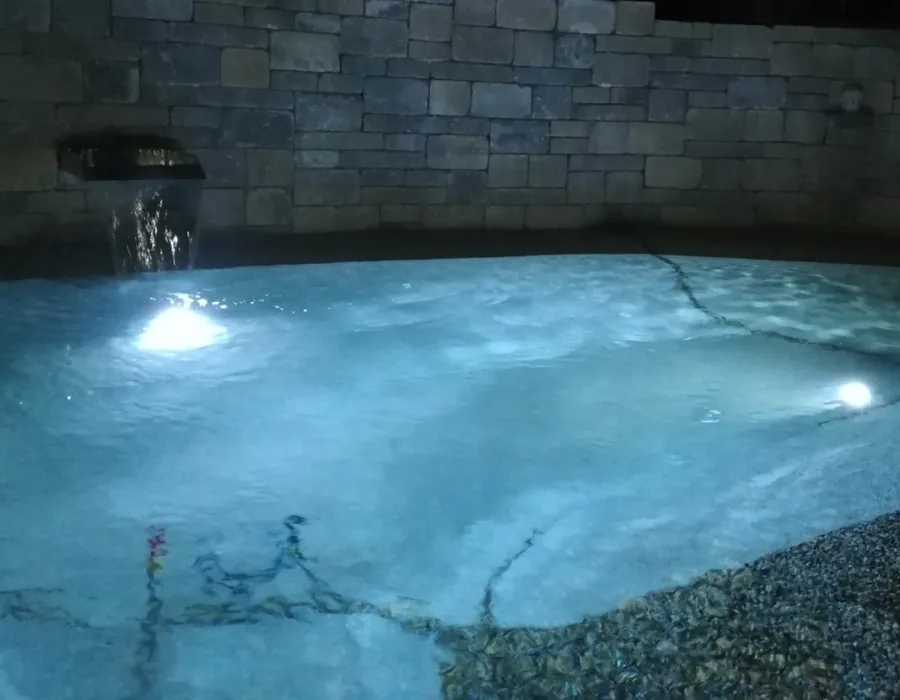 Beleuchteter BIOdesign-Pool am Abend vor einer Natursteinmauer