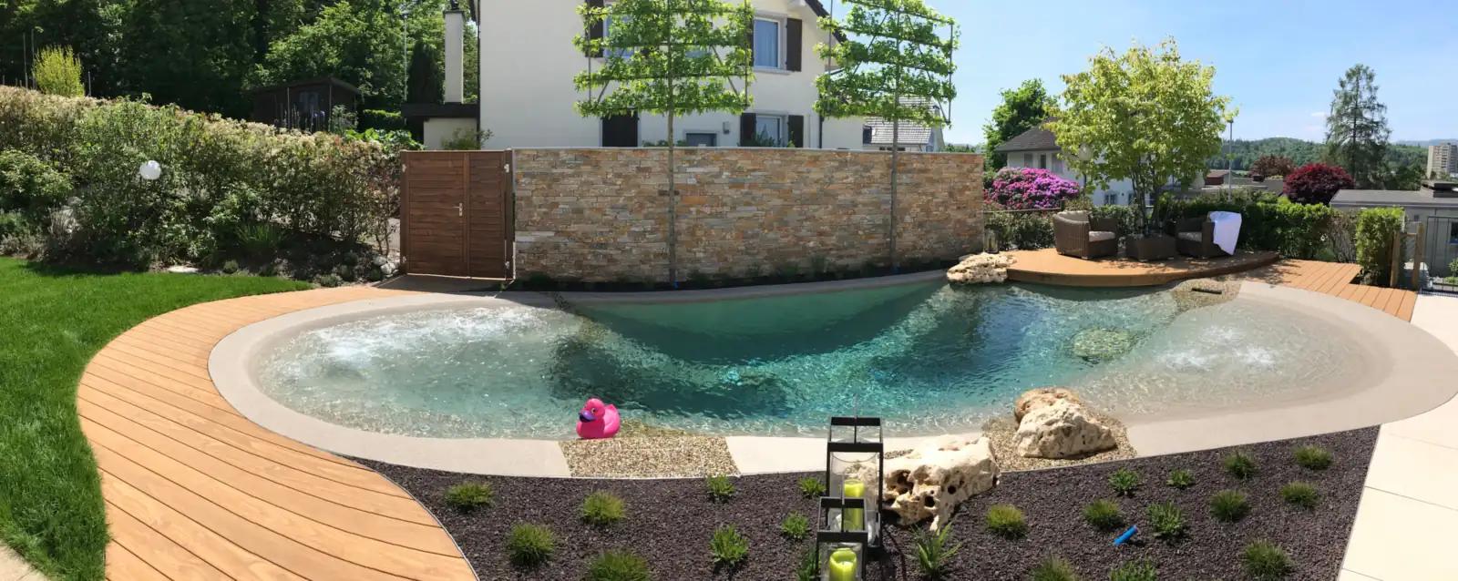 BIOdesign-Strandpool mit geschwungenem Holzdeck, Naturstein und Laternen