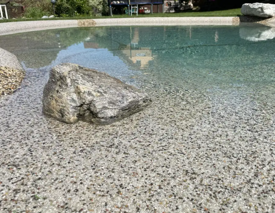 BIOdesign-Pool mit klarem Wasser über Kiesboden und Findling