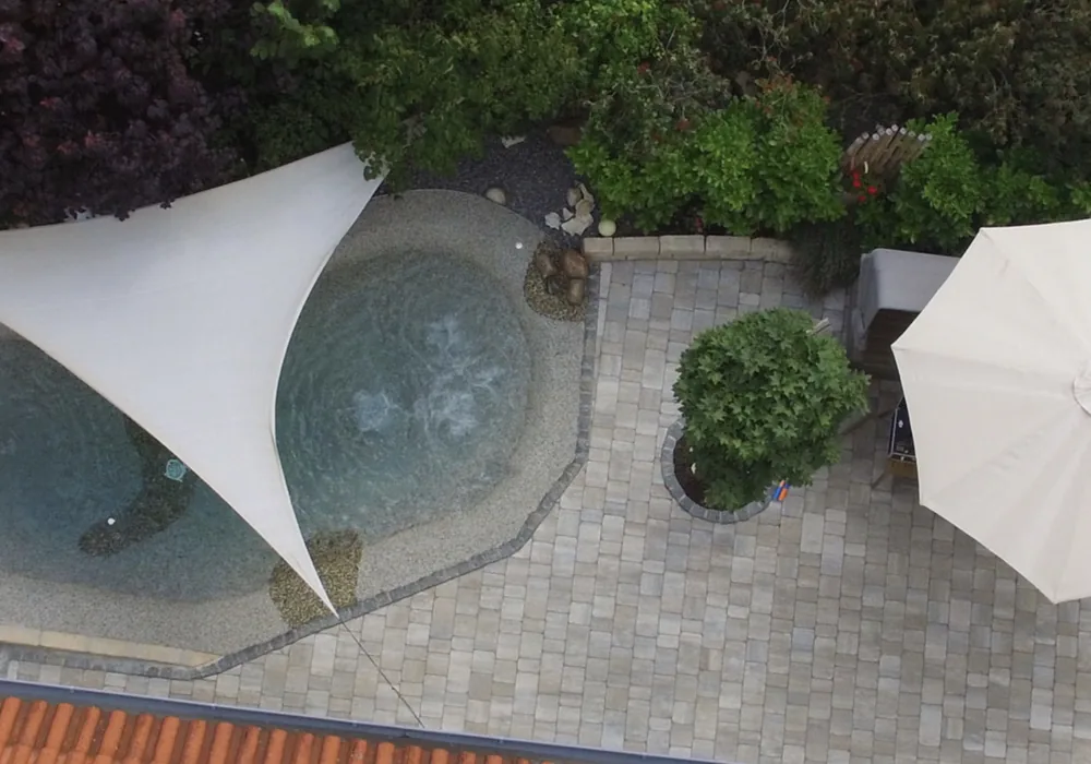 Luftbild eines BIOdesign-Pools mit Sonnensegel und Pflasterterrasse