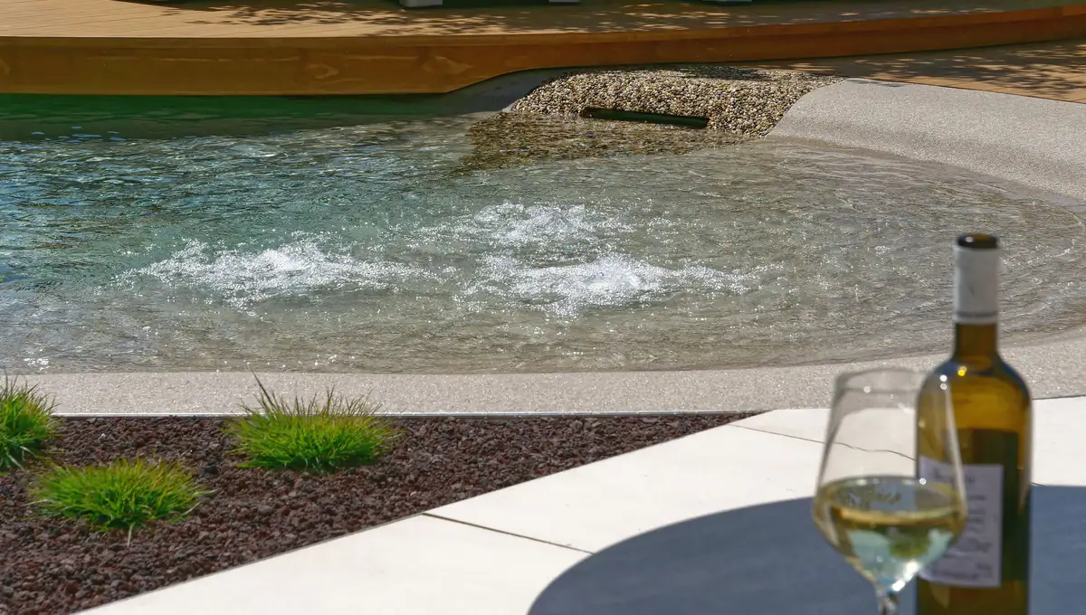 Strandpool mit Massagedüsen, Kiesbett und Weinglas am Beckenrand