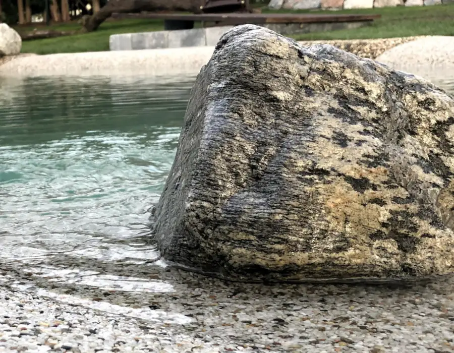 Großer Naturstein im flachen Strandbereich eines Pools