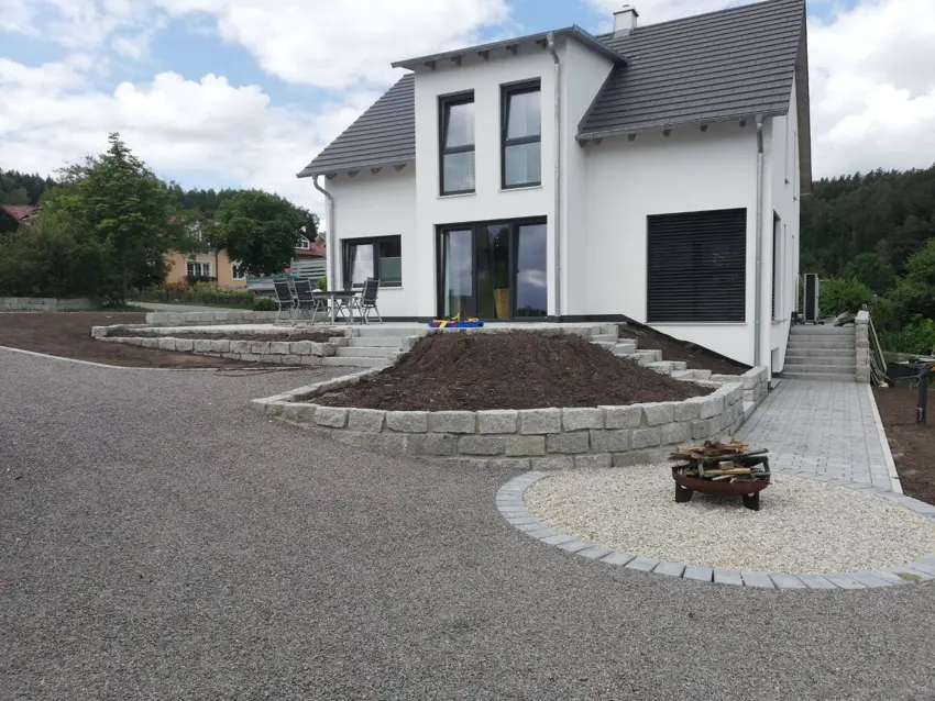 Pflasterwege und Natursteinmauern rund um ein Wohnhaus, gestaltet von Mitschke